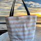 Striped tote bag with black handles on a beach at sunset