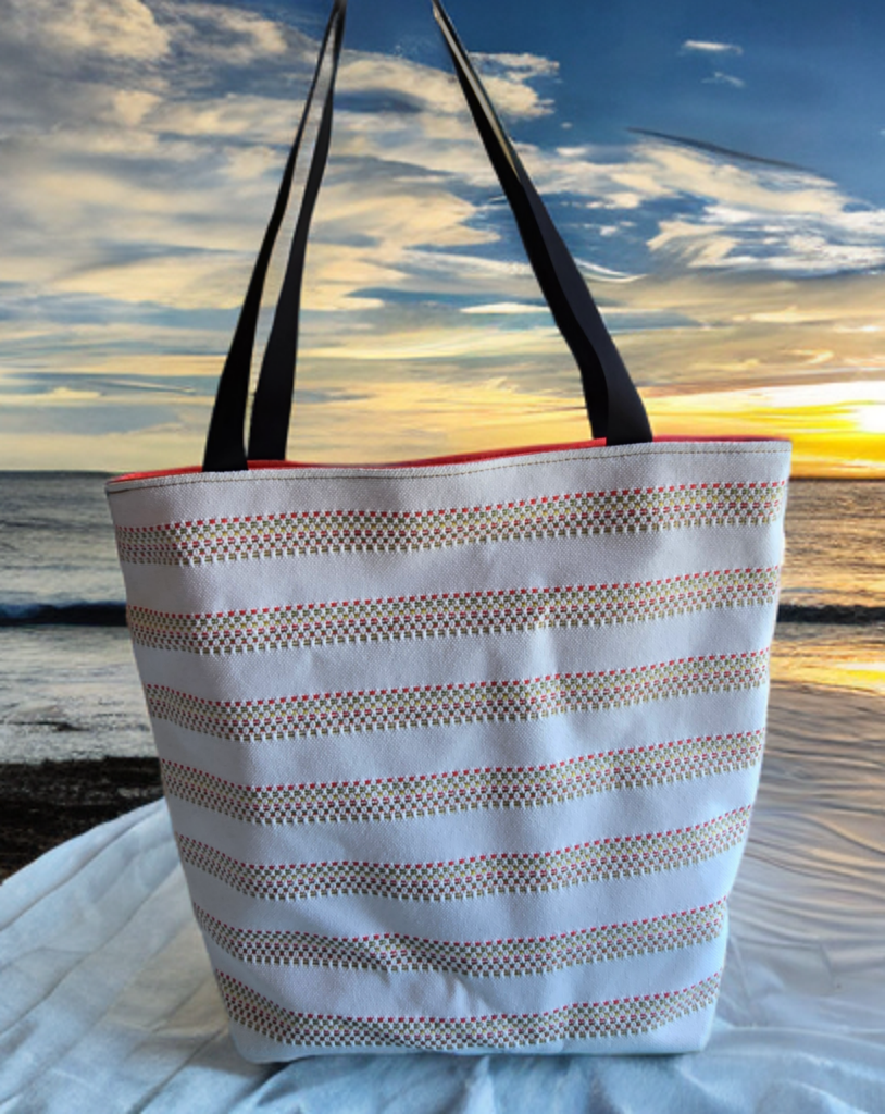 Striped tote bag with black handles on a beach at sunset