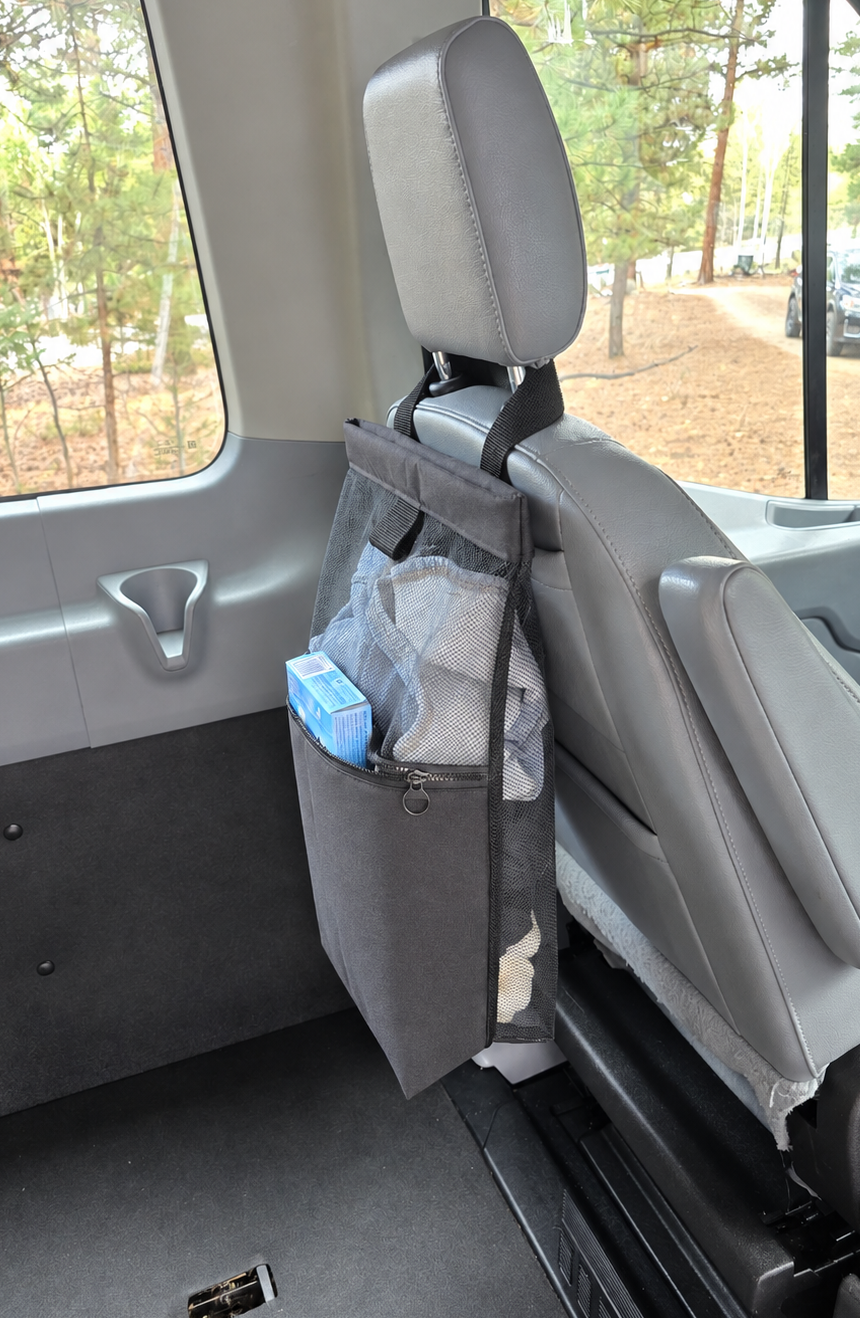A black seat back bag hanging from the headrest of a gray vehicle seat, shown inside a van  used as a laundry bag.