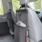 A black seat organizer hanging from the headrest of a light gray vehicle passenger seat, shown inside a van with the floor and rear area visible.