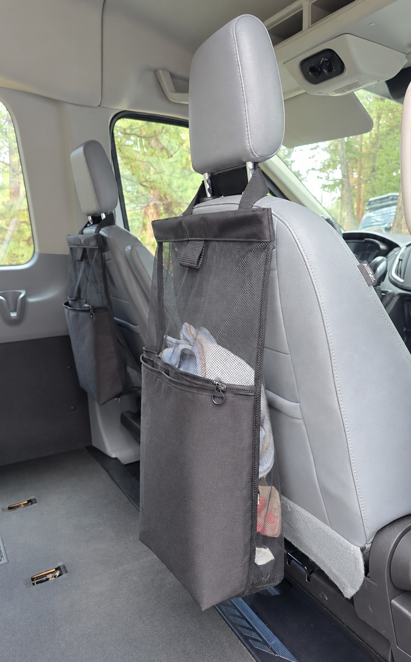 A black seat organizer hanging from the headrest of a light gray vehicle passenger seat, shown inside a van with the floor and rear area visible.