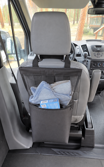 black mesh laundry bag hanging from the back of a front passenger seat inside a van, holding a light blue towel and a small blue item.